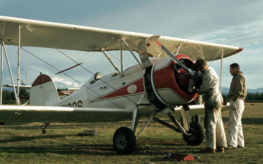 Mechanic working on the biplane engine in a grass field