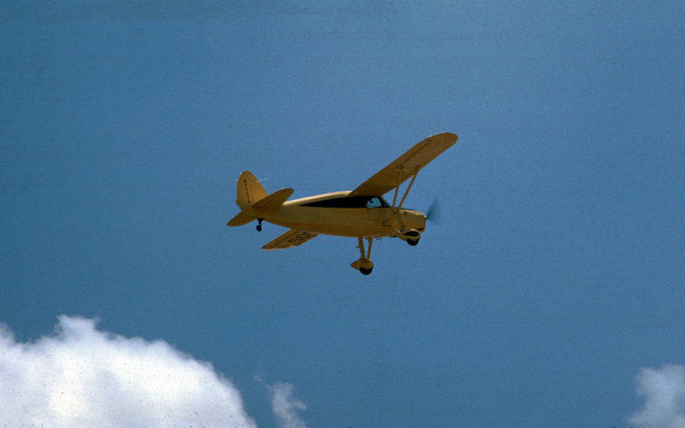 Yellow Fairchild taking off with puffy clouds and blue sky